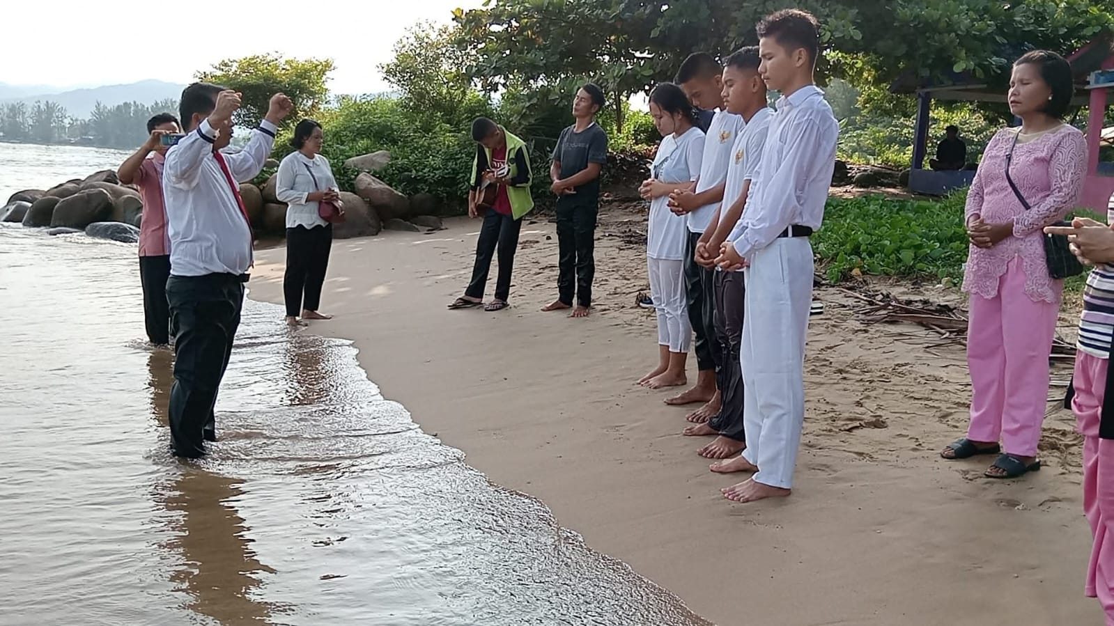 Peserta baptisan air berdoa di tepi pantai sebelum dibaptis