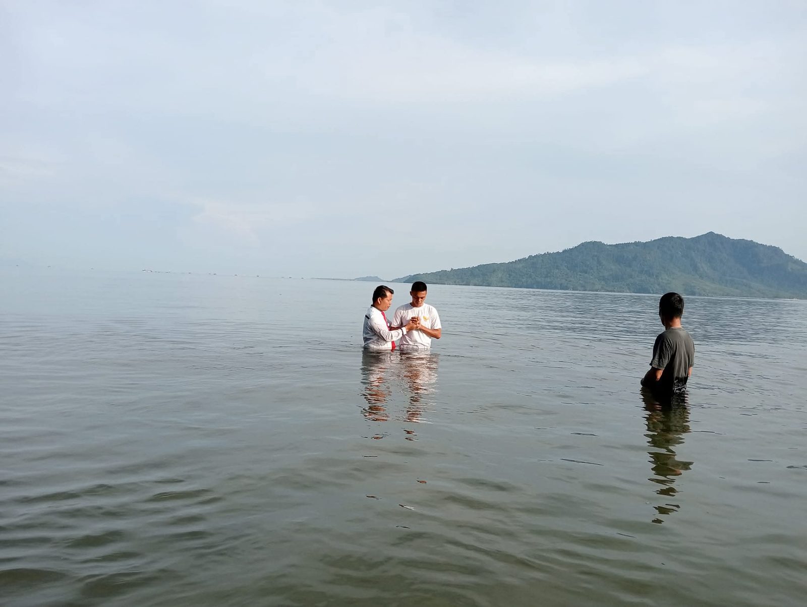 Gembala sidang membaptis jemaat di laut